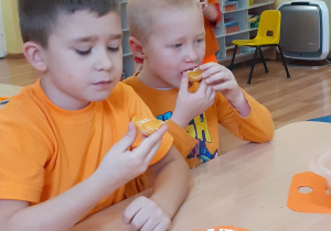 2 chłopców je pomarańczowe przekąski: mandarynki i marchewki.